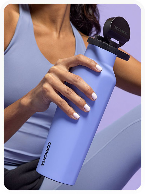 Person holding a matte lavender Corkcicle water bottle with a black lid, dressed in light blue athletic clothing.